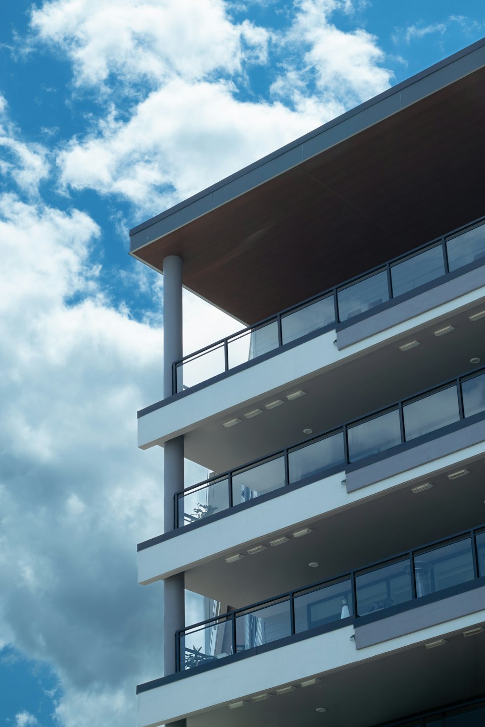 Modern apartment building with glass balconies under a blue sky.